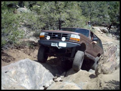 1993 Ford Bronco - A brown 1993 Ford Bronco tackles a challenging rocky terrain on an off-road trail.