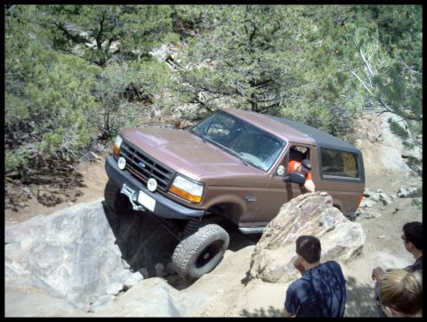 1993 Ford Bronco - A 1993 Ford Bronco maneuvers over large rocks on a challenging off-road path.