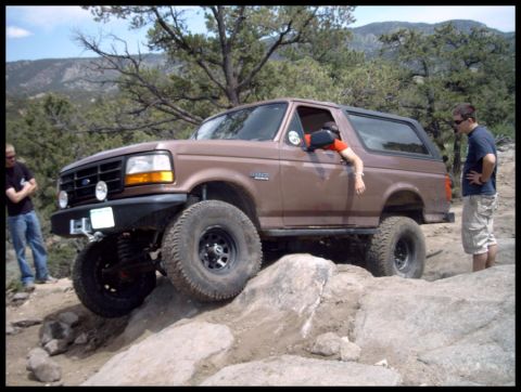 1993 Ford Bronco - A brown Ford Bronco navigates a challenging rocky trail with two people observing.
