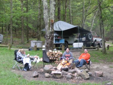 1996 Ford Bronco - People enjoy a campfire at a campsite with multiple vehicles and camping equipment.