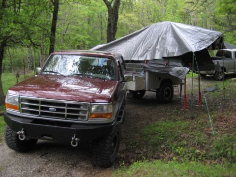 1996 Ford Bronco - A maroon Ford F-Series truck is parked next to a pop-up camper in a wooded area.