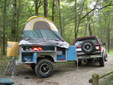 1996 Ford Bronco - A Ford Bronco tows a custom camping trailer equipped with a tent and storage compartments in a wooded area.