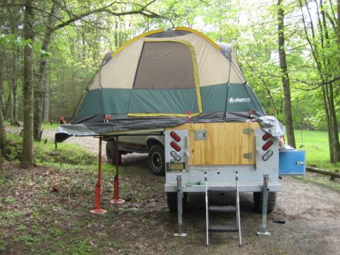 1996 Ford Bronco - A truck camper with a tent set up in a wooded area, showing the rear of the camper and a portion of the truck.