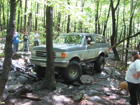 1991 Ford Bronco - A Ford Bronco tackles a challenging off-road course in a wooded area.