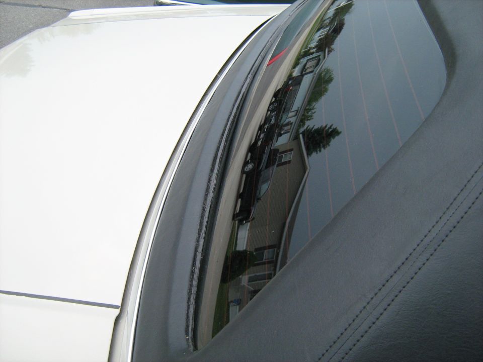 Reflection in car window shows houses and another car on a street