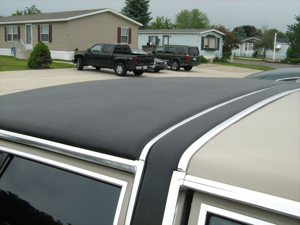 Close-up of a car's vinyl roof with chrome trim. Two trucks and an SUV are parked in the background