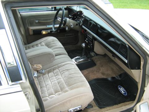 1988 Mercury Grand Marquis - The interior of a car features plush velour seats and Ford-branded floor mats.
