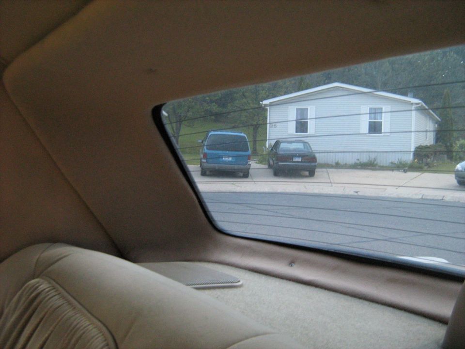 View from inside a car looking out at a blue van and a dark sedan parked in front of a mobile home