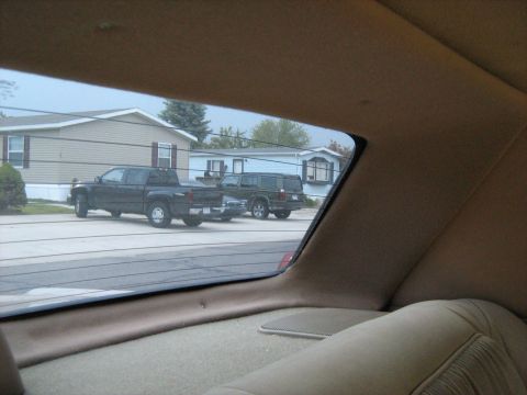 1988 Mercury Grand Marquis - Two vehicles are parked on a street in front of houses, seen through a car window.