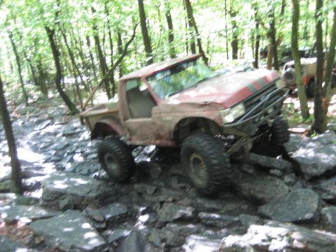 1991 Ford Bronco - This heavily modified pickup truck is navigating a rocky trail in a wooded area.