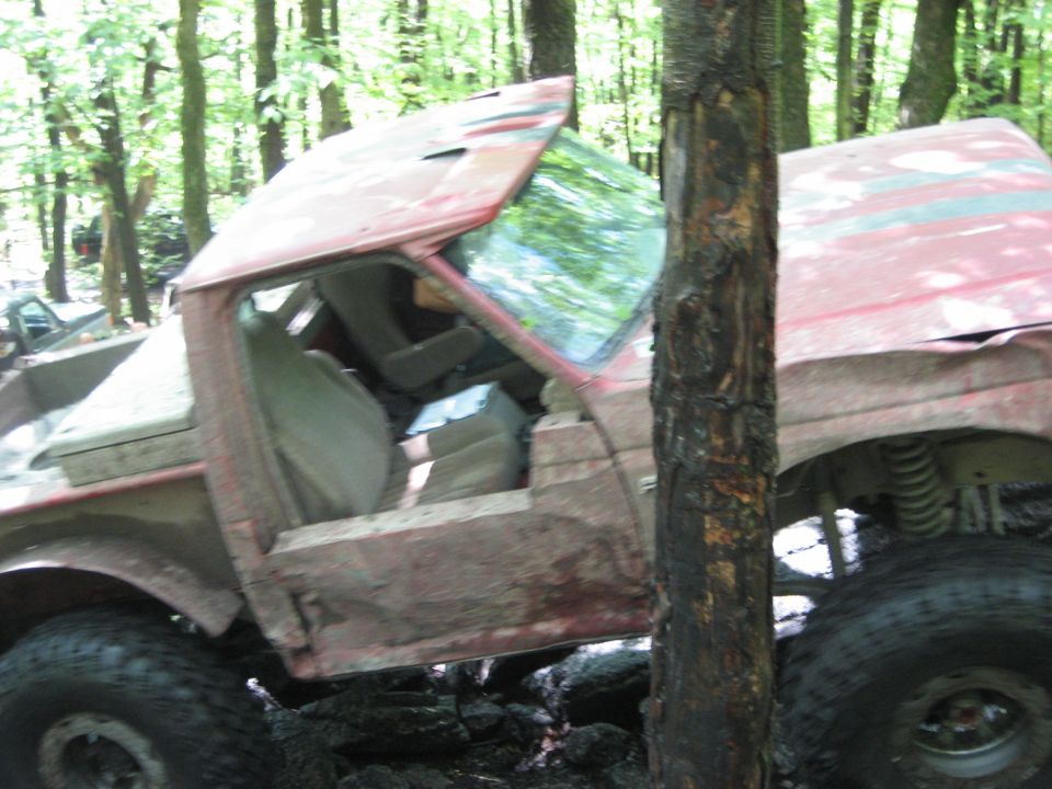 Red 1991 Ford Bronco with a damaged roof and doors, stuck in mud and rocks