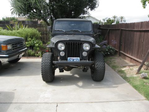 1986 Ford Bronco - A black Jeep CJ is parked in a driveway next to a Ford truck, with a wooden fence in the background.