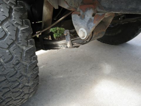 1986 Ford Bronco - Close-up view of a vehicle's leaf spring suspension and tire, with visible rust on the suspension components.