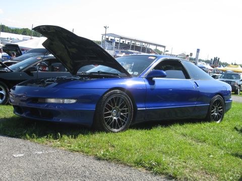 1994 Ford Probe - A blue 1994 Ford Probe is parked on grass with its hood open, showing other vehicles in the background.