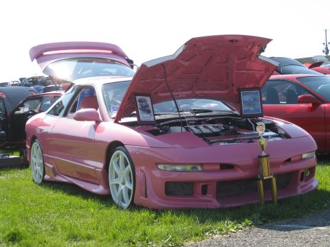 1994 Ford Probe - A pink 1994 Ford Probe is displayed with its hood and trunk open, alongside a trophy and other vehicles.
