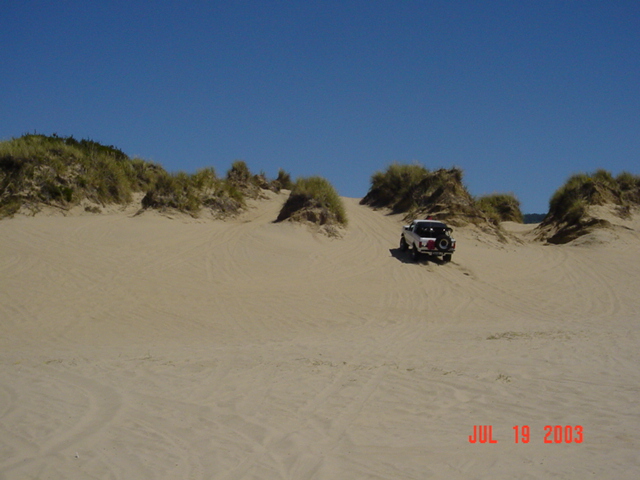 White lifted SUV with rear spare tire parked on a sand dune, tracks in sand