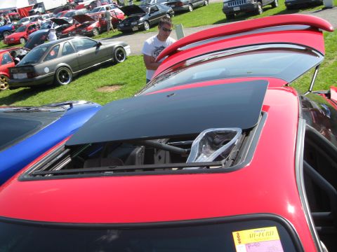 1994 Ford Probe - A red car's sunroof is open, revealing the interior mechanism. Multiple vehicles are parked on grass.