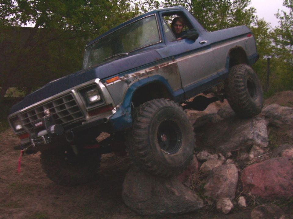 Blue and silver 1978 Ford Bronco with large tires climbing over rocks