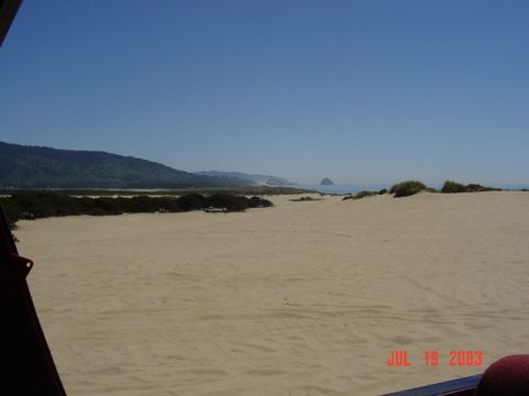1989 Ford Bronco - A wide expanse of sand dunes stretches towards the ocean under a clear blue sky.