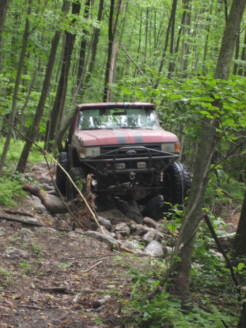 1991 Ford Bronco - A modified red Ford Bronco navigates a challenging rocky path through a dense forest.