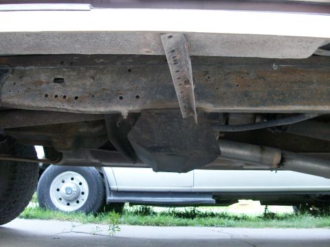 1995 Ford C-350 (Centurion Conversions) - The underside of a vehicle shows a rusty frame, fuel tank, and exhaust system.