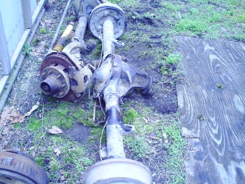 1990 Ford Bronco - Several vehicle axles and suspension components are laid out on the ground, with the Supermotors.net logo in the lower right corner.
