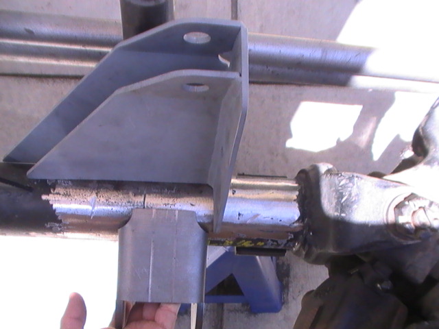 Close-up of a metal bracket being welded onto a cylindrical axle or tube, with a hand visible