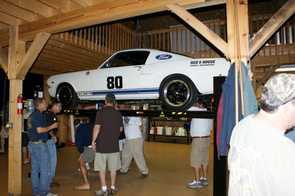 White Ford Mustang with blue stripes and number 80 on side, lifted on a car hoist