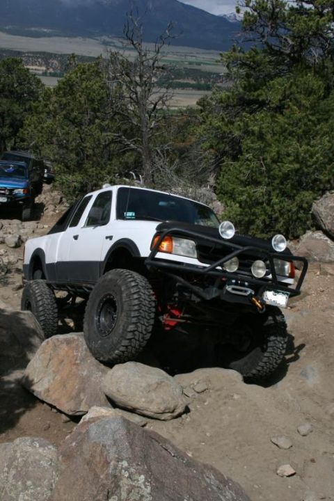 1993 Ford Bronco - Modified pickup truck navigates a rocky off-road trail with a blue SUV behind it.