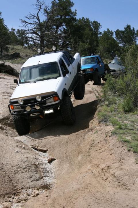 1993 Ford Bronco - Multiple off-road vehicles traverse a challenging dirt path under a clear blue sky.