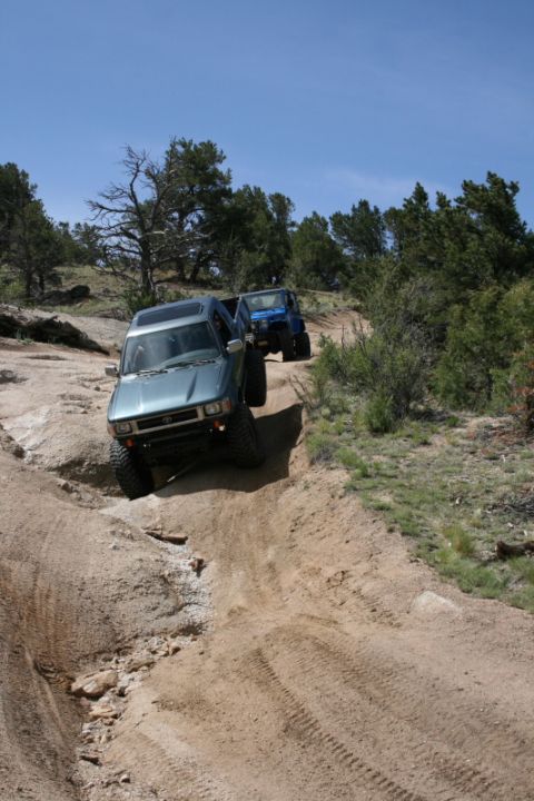 1993 Ford Bronco - Two SUVs tackle a challenging off-road trail under a clear blue sky.