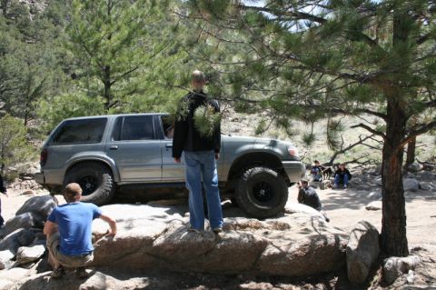 1993 Ford Bronco - A silver SUV navigates a rocky terrain with several people observing the off-road activity.