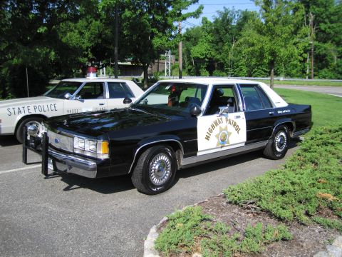 1991 Ford LTD Crown Victoria - black-and-white California Highway Patrol Ford LTD sedan is parked beside a cream Rhode Island State Police car on a lot.