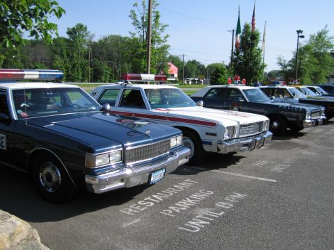 1991 Ford LTD Crown Victoria - row of vintage police sedans, including a dark Chevrolet Caprice in front, lines a lot painted RESTAURANT PARKING UNTIL 8 PM.