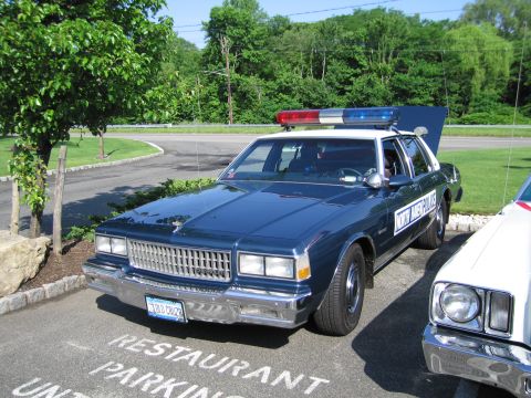 1991 Ford LTD Crown Victoria - dark blue vintage Chevrolet Caprice lettered NY State Police, with roof lightbar, parks over a RESTAURANT PARKING lot marking.