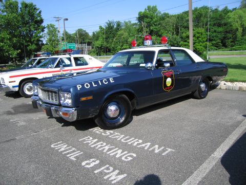 1991 Ford LTD Crown Victoria - dark blue vintage POLICE sedan with a gold badge emblem and red roof beacons is parked over a RESTAURANT PARKING UNTIL 8 PM marking.