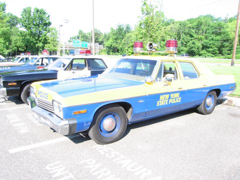 1991 Ford LTD Crown Victoria - blue-and-yellow vintage Dodge sedan lettered New York State Police, with red roof beacons, is parked in a lot among other cars.