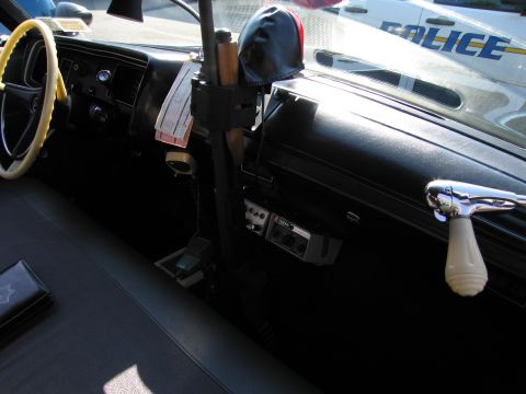 1991 Ford LTD Crown Victoria - Interior of a vintage police car with a yellow steering wheel, dashboard, radio gear, and a citation book on the seat.