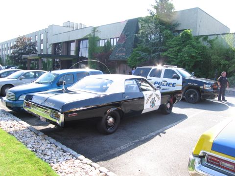 1991 Ford LTD Crown Victoria - black-and-white vintage Highway Patrol sedan and a modern Police Crown Victoria are parked outside a low building.