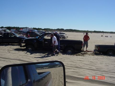 1989 Ford Bronco - Several trucks are stuck in the sand on a sunny day at the beach.