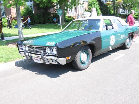 1991 Ford LTD Crown Victoria - green-and-black vintage four-door police cruiser with push bumper and roof light, numbered 7468, at an outdoor show.