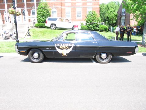 1991 Ford LTD Crown Victoria - black State Highway Patrol cruiser with a winged door emblem and red roof light parked in front of a brick building.