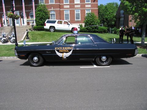1991 Ford LTD Crown Victoria - Side profile of a black State Highway Patrol four-door sedan with gold winged door emblem and single red roof light.