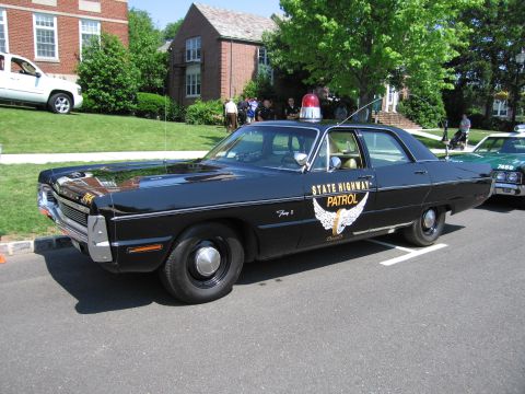 1991 Ford LTD Crown Victoria - black State Highway Patrol cruiser with winged gold door emblem and red roof beacon parked among other show cars.