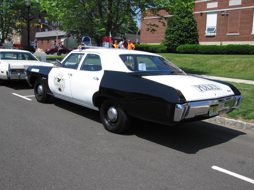 Rear three-quarter of black and white POLICE sedan with shield door emblem