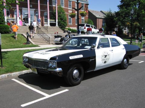1991 Ford LTD Crown Victoria - black-and-white four-door police cruiser lettered POLICE with a round door emblem parked in front of a brick building.