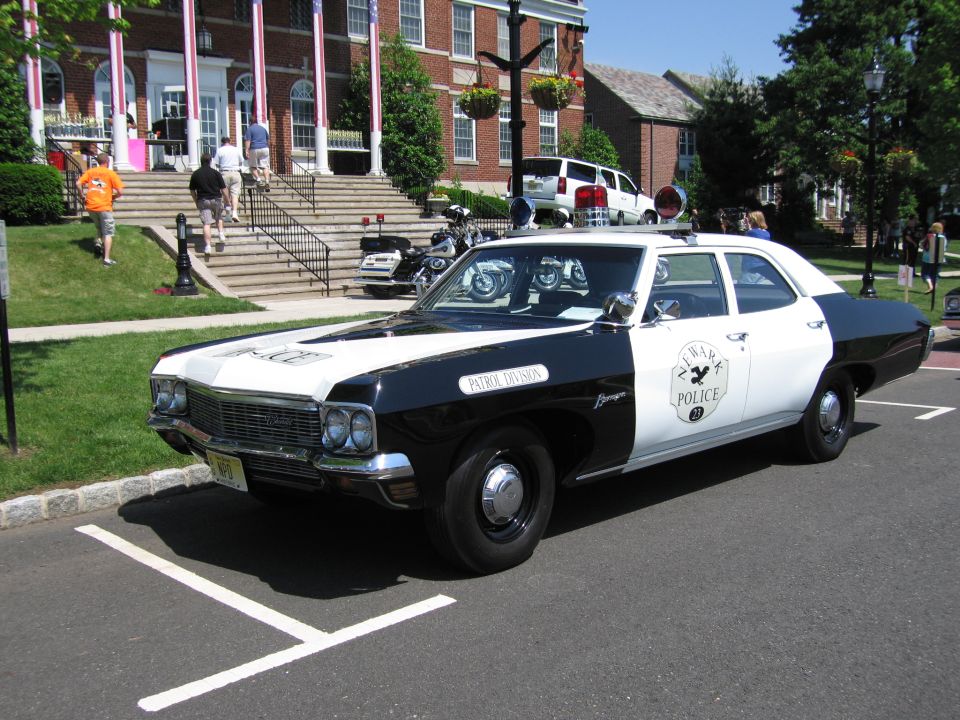 Front three-quarter of black and white POLICE sedan with circular door emblem