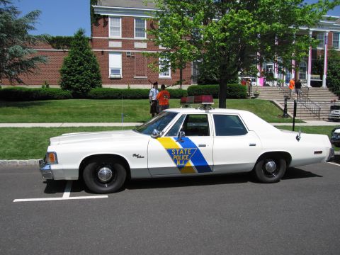1991 Ford LTD Crown Victoria - white New Jersey State Police four-door sedan with a blue-and-yellow side stripe and roof lightbar parked on a street.