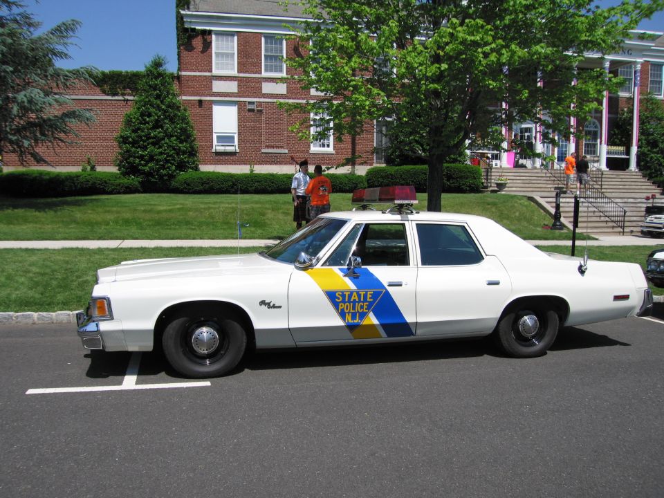 Side view of white New Jersey State Police sedan with blue and yellow stripe