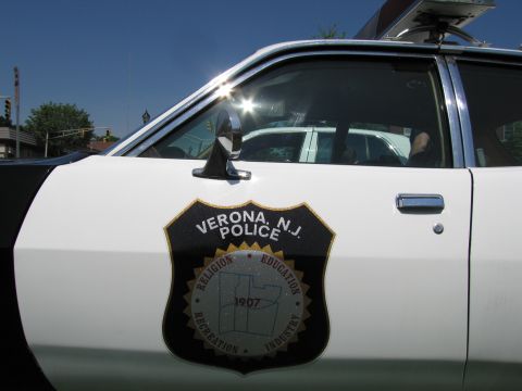 1991 Ford LTD Crown Victoria - Close-up of a black-and-white police car door bearing a Verona, N.J. Police shield emblem dated 1907 under bright sun.